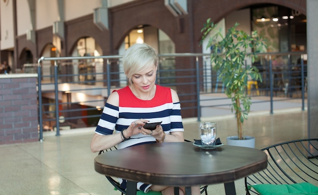 Middle aged woman sits at cafe texting or operating her smart cell phone