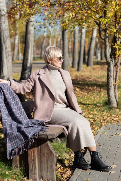 Middle-aged woman sits on a park bench in autumn. High quality photo