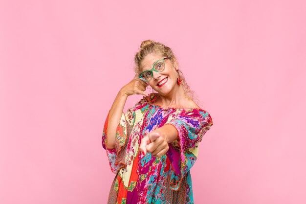 Middle aged woman smiling cheerfully and pointing to front while making a call you later gesture, talking on phone