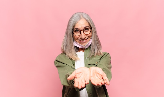 Middle aged woman smiling happily with friendly, confident, positive look, offering and showing an object or concept