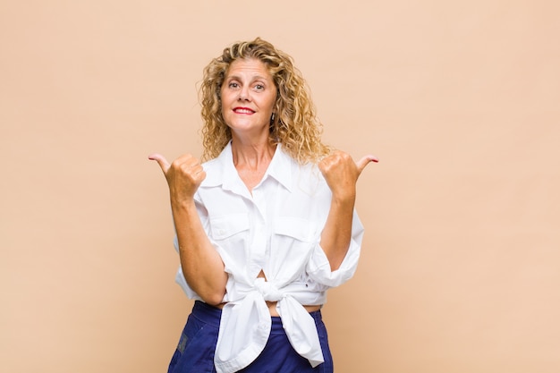 Middle aged woman smiling joyfully and looking happy, feeling carefree and positive with both thumbs up