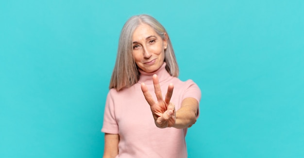 Middle aged woman smiling and looking friendly, showing number three or third with hand forward, counting down