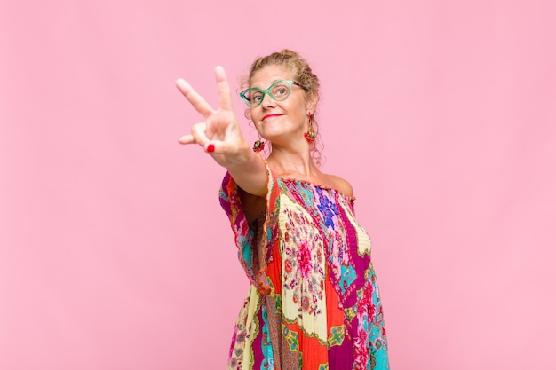 Middle aged woman smiling and looking happy, carefree and positive, gesturing victory or peace with one hand