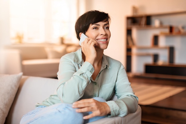 Middle aged woman speaking on mobile phone communicating at home