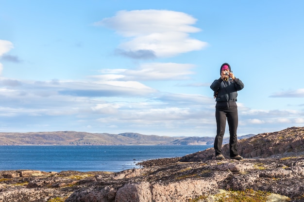 Женщина средних лет фотографирует стоя на скале