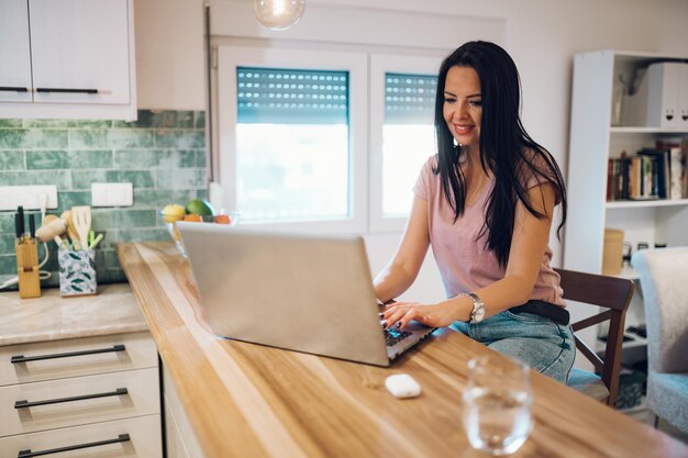 Middle aged woman using laptop while sitting at kitchen counter at home