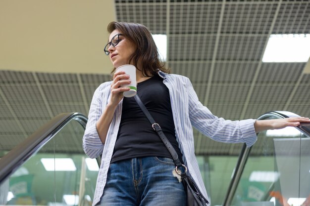 Donna di mezza età con la tazza di caffè nel centro commerciale