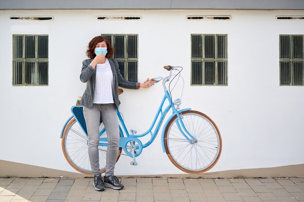 Middle-aged woman with face mask leaning against a wall with painted bicycle