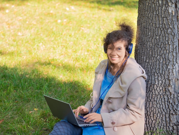 Middle aged woman with laptop in city park looking at camera and smiling