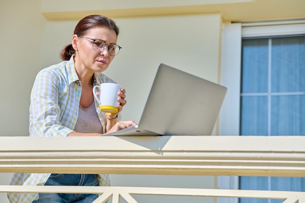 Middle aged woman with laptop on the porch of the house