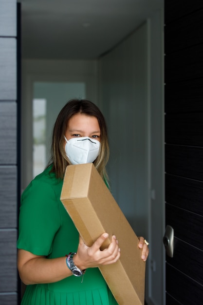 Middle-aged woman with a mask picking up a package at home