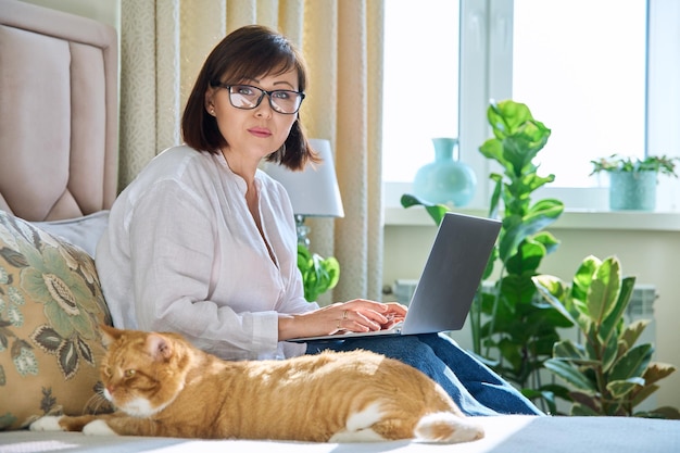 Middle aged woman working from home using laptop looking at camera