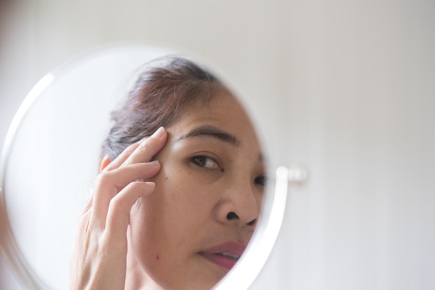 Middle-aged women are looking at the mirror to see the facial wrinkles.  