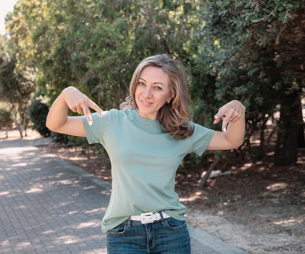 TシャツとTシャツを指してジーンズを着ている中年の女性は公園で屋外に滞在します