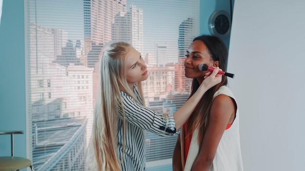 Middle closeup of makeup artist applying makeup on beautiful mixedrace model during photo shoot in m...