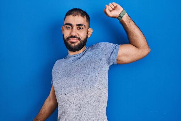 Middle east man with beard standing over blue background stretching back, tired and relaxed, sleepy and yawning for early morning