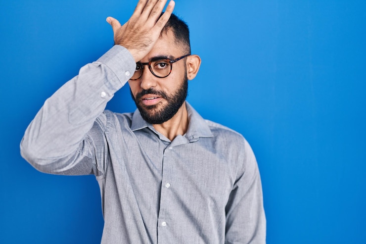 Photo middle east man with beard standing over blue background surprised with hand on head for mistake remember error forgot bad memory concept