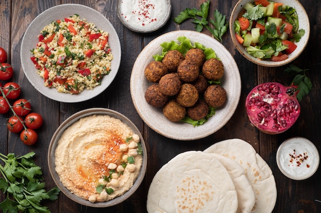 Middle eastern or arabic cuisines falafel hummus tabouleh pita and vegetables on wooden background view from above