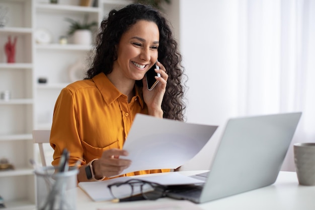 Middle eastern businesswoman talking on phone holding papers in office