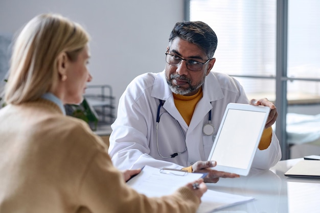 Photo middle eastern doctor showing tablet with white screen to patient