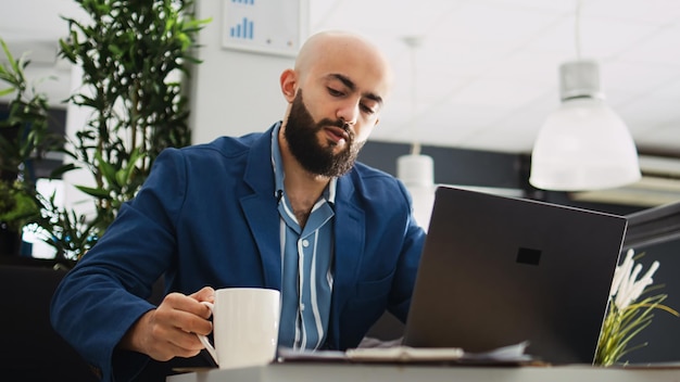 Photo middle eastern man reads documents online before creating professional marketing report in office. male worker trying to find business solution, entrepreneur in coworking space.