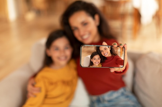 Middle eastern mom and daughter making selfie via phone indoor