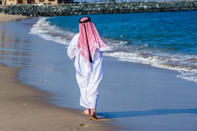 중동 방식으로 옷을 입고 아랍 사람 바다 해안 앞 포즈.