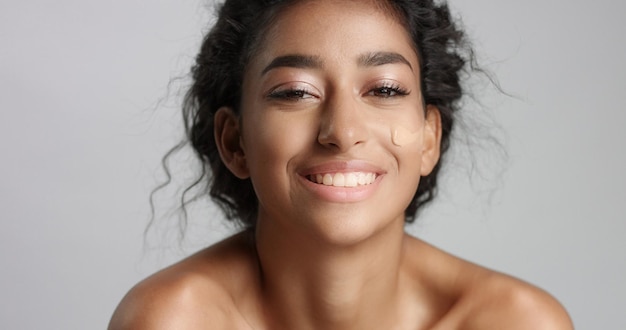 Middle eastern young woman in studio with a foundation on cheek closeup Touching skin