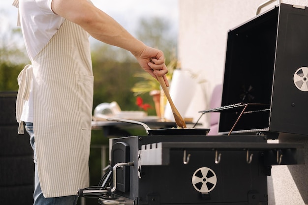 Middle selection of man in apron using wooden spoon to mix vegetables on frying pan Prepare food on grill