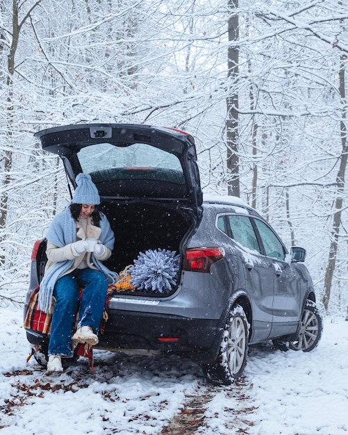 in middle of winter forest young woman sits in trunk of car with christmas tree