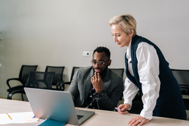 Photo middleadult female boss mentor helping black male employee with online assignment teach intern in