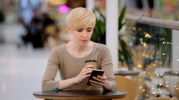 Middleaged adult woman caucasian lady with short haircut sitting at cafe table drinking coffee tea