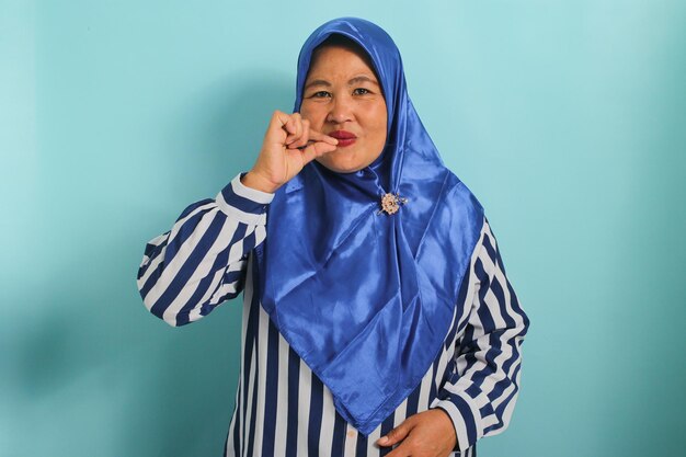 写真 青いヒジャブを着た中年のアジア人女性が口を動かし、秘密を守り、青に隔離