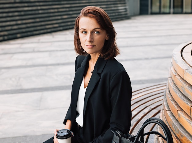 Photo middleaged business woman sitting outdoors during lunch holding coffee