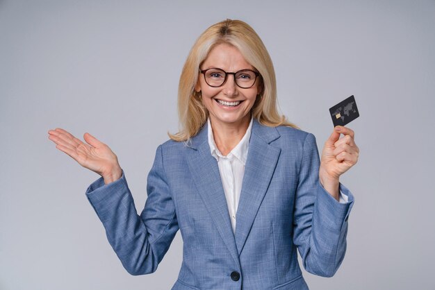 Middleaged business woman with credit card in formal attire isolated over grey background