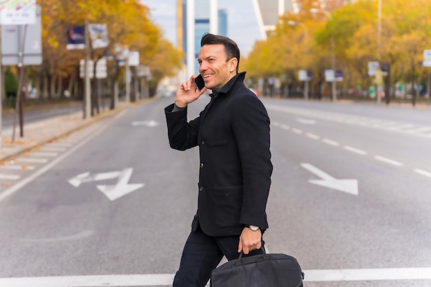 Middleaged Caucasian businessman talking on the phone crossing the road in the city