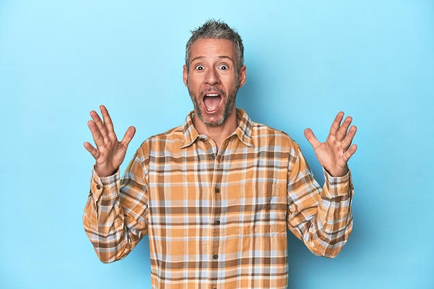 Middleaged caucasian man on blue backdrop celebrating a victory or success