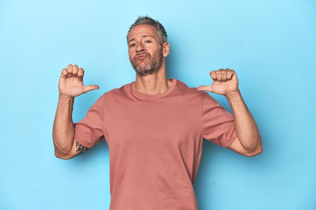 Middleaged caucasian man on blue backdrop feels proud and self confident example to follow