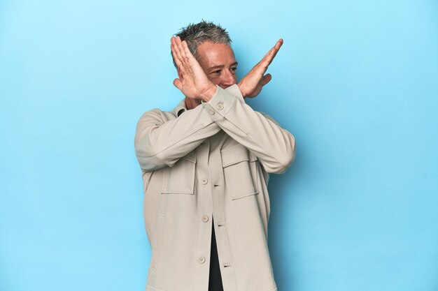 Middleaged caucasian man on blue backdrop keeping two arms crossed denial concept