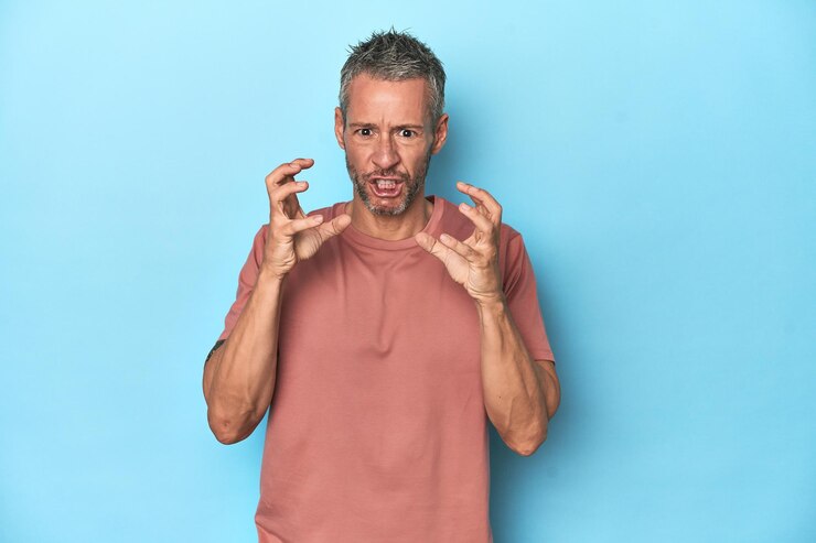 Photo middleaged caucasian man on blue backdrop upset screaming with tense hands