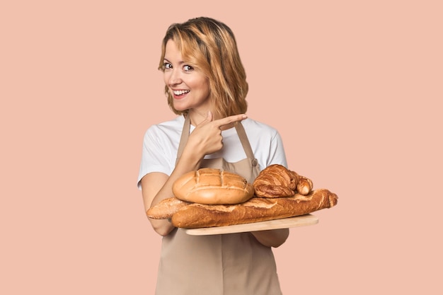 Middleaged Caucasian woman baker with bread tray smiling and pointing aside