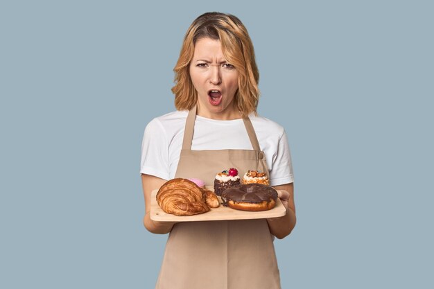 Middleaged Caucasian woman baker with pastries screaming very angry and aggressive