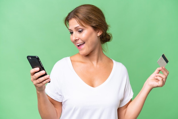 Middleaged caucasian woman over isolated background buying with the mobile with a credit card