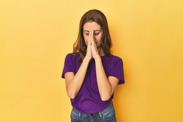 中年の白人女性が黄色で手を握って口の近くで祈り 自信を持っています