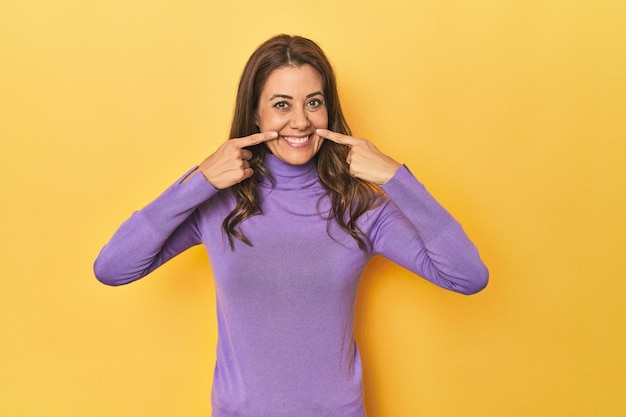 middleaged caucasian woman on yellow smiles pointing fingers at mouth