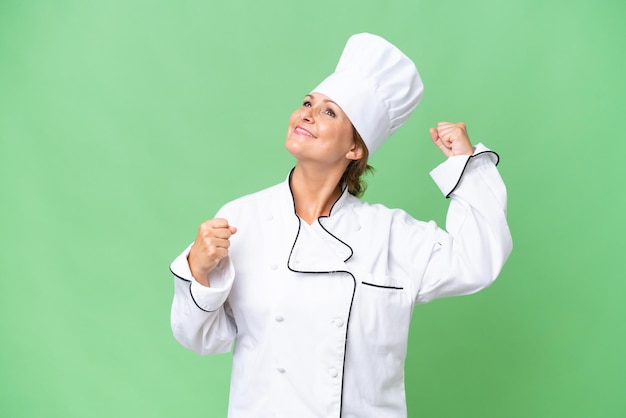 Middleaged chef woman over isolated background celebrating a victory