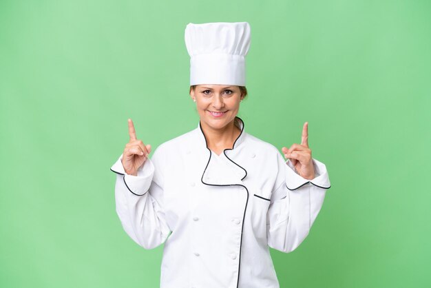 Middleaged chef woman over isolated background pointing up a great idea