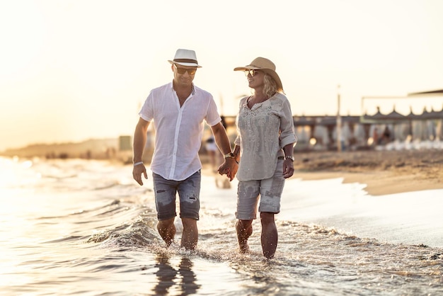 A middleaged couple walking hand in hand on the beach at sunset