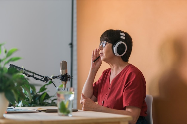 Middleaged female radio presenter talking into the microphone and reading news radio broadcast online concept