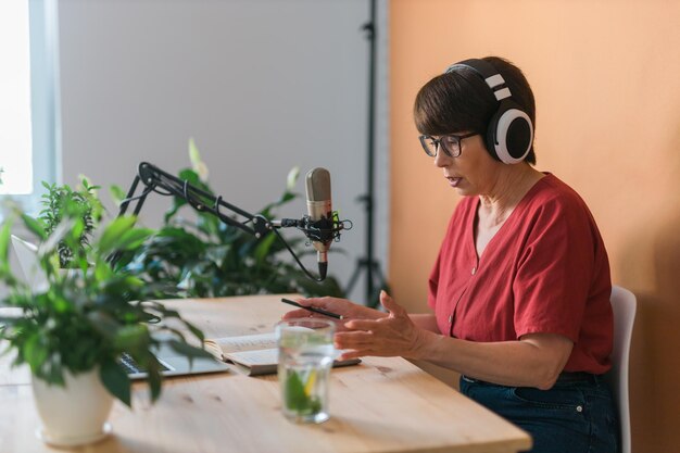 중년 여성 라디오 발표자가 마이크에 대고 뉴스 라디오 방송을 읽고 있습니다.